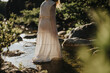 © qunica.com - A woman wearing a long white dress stands in a tranquil forest stream, capturing a moment of serenity and nature's beauty.