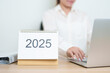 © Jo Panuwat D - 2025 Year Calendar on table with business woman using laptop computer, working and writing in office. countdown, Happy New Year, Resolution, Year End and New Start and Goals Plan Action Concept