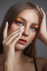 Wall Mural - young woman showcases her unique style with bold eye makeup featuring vibrant warm hues while gently touching her face. This stylish look highlights her artistic expression in a studio