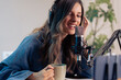 © Lomb - Young female podcast host enjoying coffee break during content recording session with professional microphone in creative home studio