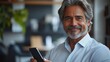 © lai - A smiling man with gray hair holds a smartphone, exuding confidence in a modern setting.