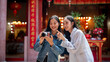 © bongkarn - Two happy, pretty Asian female friends visit a Chinese shrine, checking photos on a camera together.