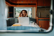 © Halfpoint - Woman is camping in nature, sitting in her caravan and working on a notebook. Caravan as homeoffice, working remotely.