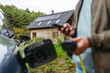 © Halfpoint - Man charging electric car in front of his house, plugging the charger into the charging port. House with solar panel system on roof behind him.
