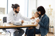 © sofiko14 - Caucasian doctor measures temperature of little sick girl on woman's lap. Scene set in medical office with professional consultation.