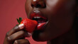 © Helga P-A. - Close-up of a Black woman's sensual lips with glossy red lipstick about to take a bite of a fresh, ripe strawberry. Concept of beauty, sensuality, and indulgence.