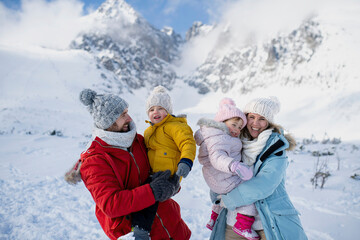 Wall Mural - Young family is enjoying winter holiday in the mountains, standing in the middle of snowy landscape.