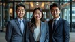© M_H_L - A diverse team of three business professionals smiling for the camera, standing in a modern office building.