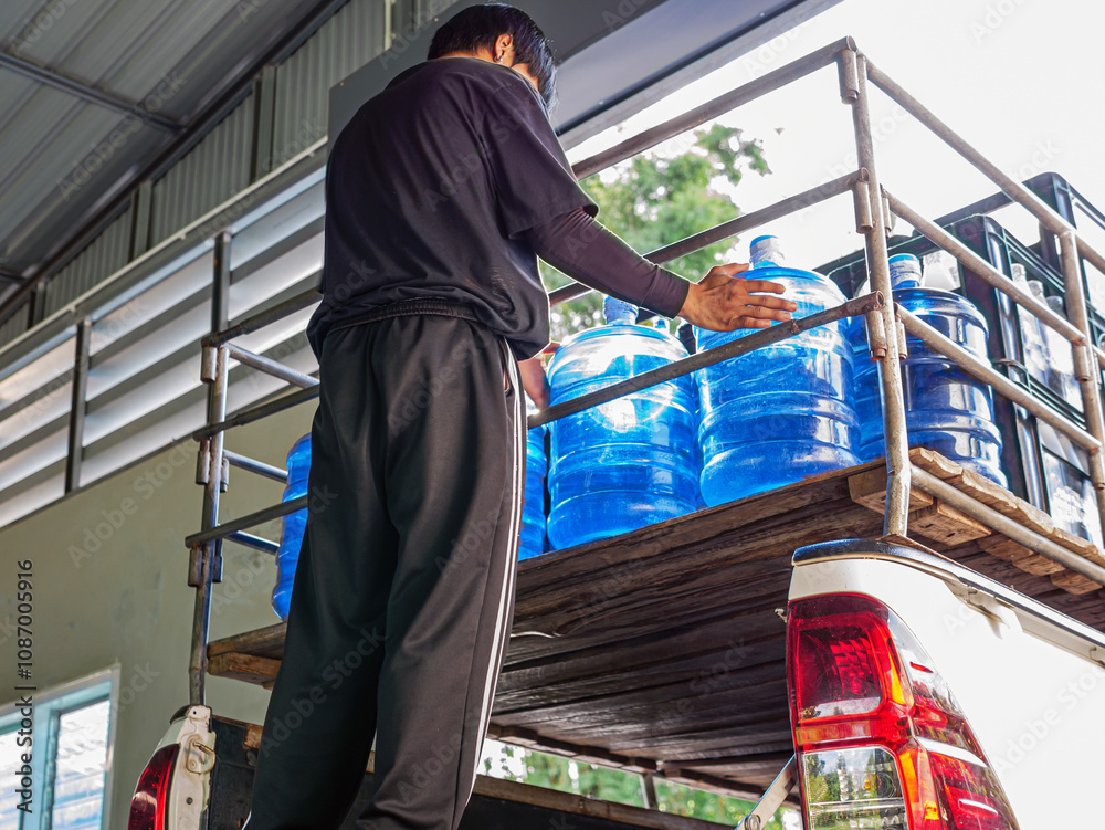 Workers lift blue drinking water gallon into the back of a transport ...