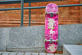 Used scratched pink skateboard against stone wall at city street. Urban sport and youth subculture concept