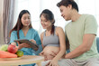 © Stella - Beautiful female nutritionist holding tablet while consulting about essential healthy foods to happy Asian family. Pregnant mother and husband listening to advice from medical nurse on improving diet.