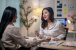 © Apichat - Two women are sitting at a desk, talking to each other