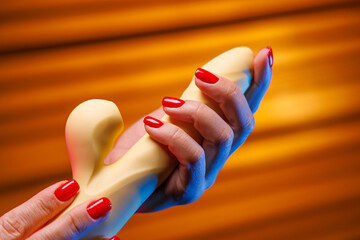 A female hand with a sensual red manicure gently holds a yellow vibrator. Neon lighting highlights the shape of the toy and creates a sensual mood for intimate play.