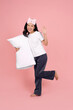 © PBXStudio - Full body photo of young Asian woman in pajamas hugging pillow and jumping isolated on pastel pink background..
