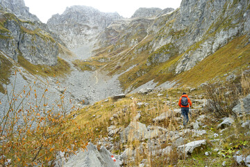 Wall Mural - A man explores the interesting places of Prokletije National Park in Montenegro: a tourist, photographed from behind, walks along a path marked with red and white marks in the Ljubokuć mountain valley