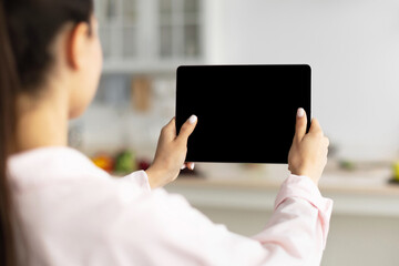 Poster - Over The Shoulder View Of Unrecognizable Woman Using Digital Tablet With Empty Screen Standing In Kitchen At Home. Application Or Internet Website Advertising, Mock Up, Free Space, Selective Focus