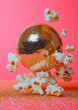 © Femmes.Digital - Golden disco ball surrounded by flying popcorn on pink background. Surreal party concept blending cinema and dance aesthetics.