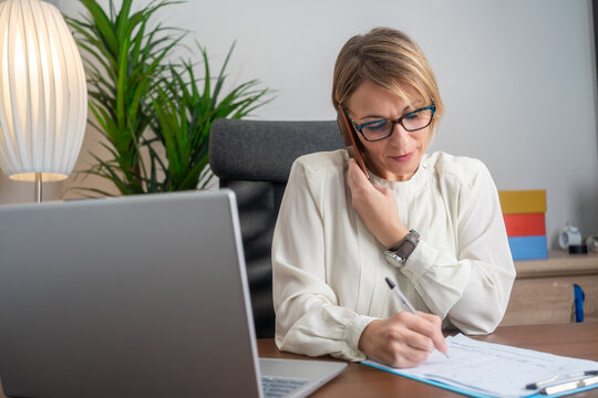 Mature businesswoman thinking about something while sitting front open portable laptop computer reading email from client, long hours of work. Creative middle aged woman working on laptop 