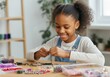 © Running opossum - Smiling preteen black girl making necklaces and bracelets, enjoying her hobby at home