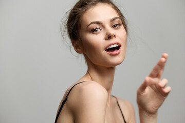 Poster - Confident young woman with a playful expression, wearing a simple black top, against a light grey background. Emphasizing joy and self-assurance in a minimalistic setting.