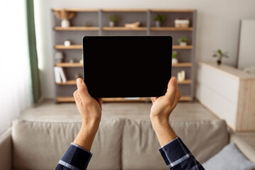 Aufkleber - Male Hands Holding Digital Tablet With Blank Screen Mockup For Website Advertisement Standing At Home. Guy Showing Computer Display Template Over Domestic Living Room Background. Selective Focus