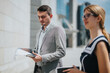 © qunica.com - Confident businessman reviews documents outdoors during a business meeting with colleague. Sunny day, urban setting, emphasizing professionalism and teamwork.