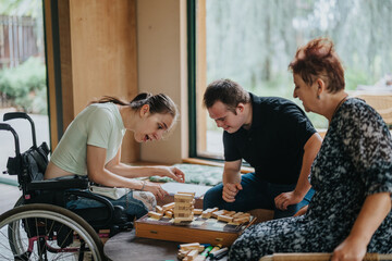 A boy with down syndrome, a girl in a wheelchair, and an elderly woman engage in a fun and inclusive building blocks game, fostering joy and connection.