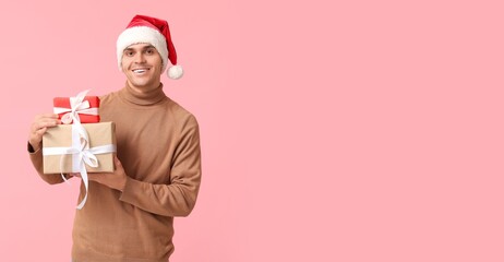 Sticker - Handsome young man in Santa hat holding Christmas gifts on pink background with space for text