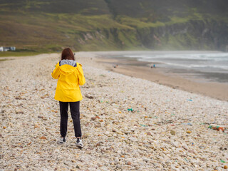 Wall Mural - A woman in a yellow jacket is walking on a rocky beach. The beach is empty and the woman is the only person in the stunning nature scene. Achill island, Ireland. Travel and tourism.