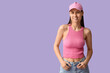 © Pixel-Shot - Beautiful young woman in stylish pink cap on lilac background