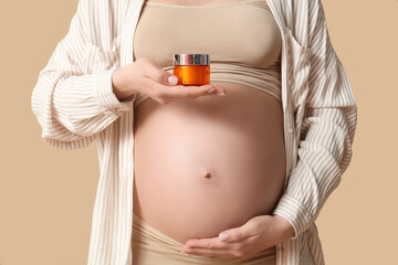 Wall Mural - Pregnant woman holding jar of cream on color background, closeup