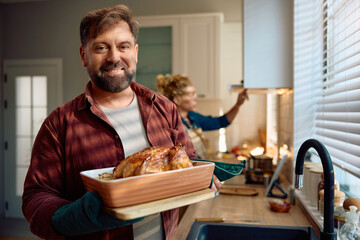 Wall Mural - Smiling man with roast turkey in kitchen looking at camera.