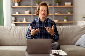 Poster - Virtual Meeting. Freelancer Man Having Video Call At Laptop Talking To Computer Webcam Wearing Headset Sitting On Sofa At Home. Distance Work, Online Communication Concept. Selective Focus