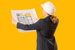 © Pixel-Shot - Young female architect with blueprint on yellow background, back view. Woman in male profession concept
