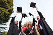 © New Africa - Graduation ceremony. Group of students with diplomas throwing hats outdoors, low angle view