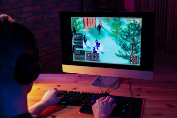 Young man playing video game with keyboard at wooden table indoors, back view