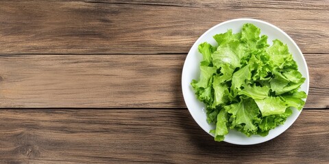 Wall Mural - Fresh lettuce leaves in a white plate on a wooden table background. Top view. Copy space.