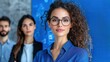 © FarhaStock - Confident Businesswoman with Curly Hair Wearing Glasses in an Office Setting, Standing in Front of Colleagues Against a Blue Background