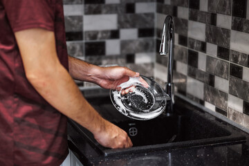 Wall Mural - person stands at a sleek kitchen sink, carefully washing a soapy plate. The kitchen features stylish tiles in shades of gray and black, creating a contemporary atmosphere. hands washing dirty dish