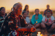 © axel - An Indigenous Two-Spirit elder conducts a sacred ceremony, holding a stick of flame, while surrounded by attentive community members at sunset, creating a connecting ambiance
