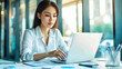 © Renuom - Asian businesswoman using laptop while analyzing reports in office.