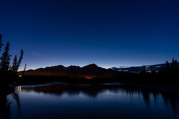 Wall Mural - Pyramid Mountain silhouette reflected on Athabasca River at twilight time. Town Jasper at night. Alberta, Canada.