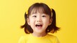 © Oleg - Portrait of happy little girl with pigtails smiling broadly at camera against a vibrant yellow background.