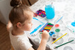 © Kiryakova Anna - A cute girl draws with paints and pencils at a table near the window.