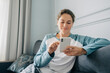 © Ilona - A beautiful brunette woman sits on the sofa and uses a mobile phone to communicate online.