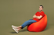 © ViDi Studio - Full body young middle eastern man wear red t-shirt casual clothes sit in bag chair hold hands crossed folded look camera isolated on plain pastel green background studio portrait. Lifestyle concept.