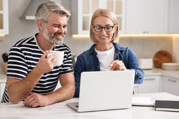 Wall Mural - Happy middle aged couple working at white marble table in kitchen