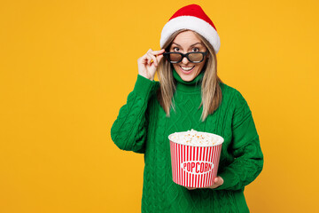 Wall Mural - Young surprised merry woman wear green sweater 3d glasses watch movie film hold bucket of popcorn in cinema isolated on plain yellow background. Happy New Year, celebration Christmas holiday concept.