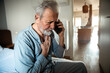 © Davor - Senior man talking on the smartphone holding chest at home