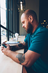 Fototapete - Young hipster guy checking new updates of social networks content via smartphone on break in cafeteria, creative male bolgger chatting with followers an share multimedia using mobile phone and wifi
